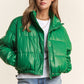 Green faux leather turtleneck crop puff jacket with zipper and snap closures, featuring a lined interior and stylish drawstring hem.