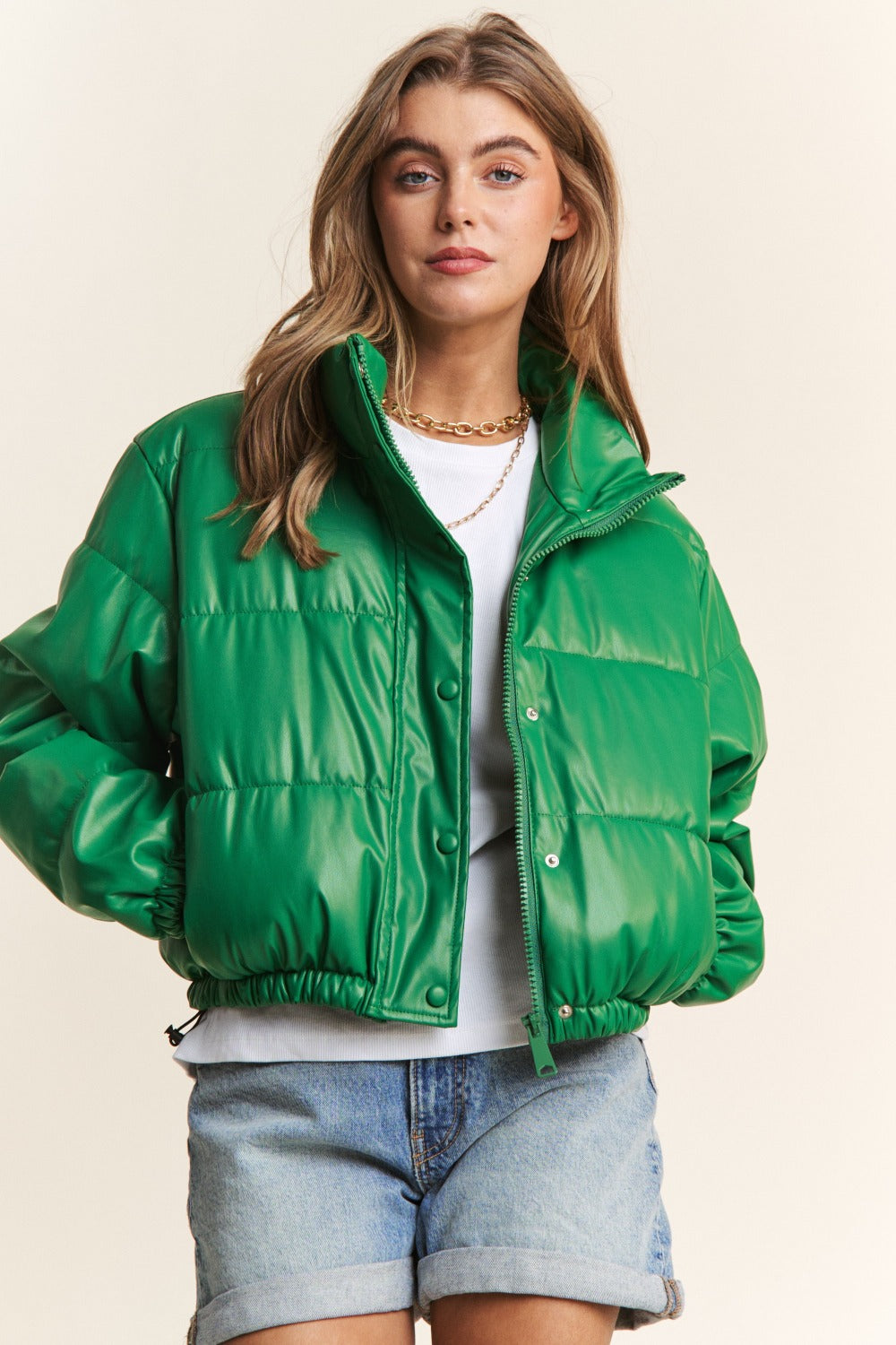 Green faux leather turtleneck crop puff jacket with zipper and snap closures, featuring a lined interior and stylish drawstring hem.