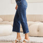 Woman wearing Tummy Control High Waist Raw Hem Distressed RFM Jeans in a living room setting.