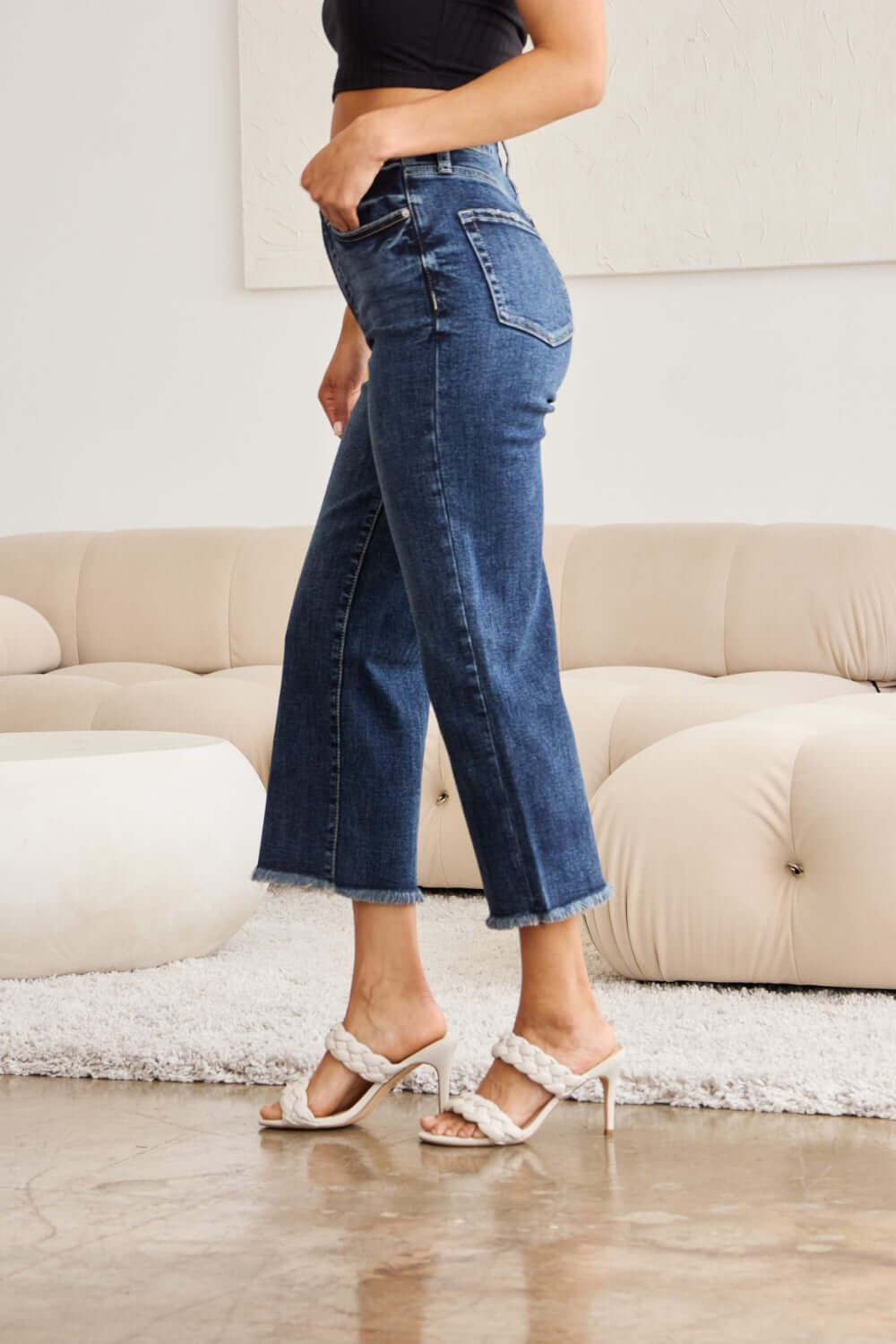 Woman wearing Tummy Control High Waist Raw Hem Distressed RFM Jeans in a living room setting.