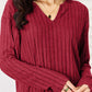 Woman wearing a burgundy ribbed notched long sleeve top from a two-piece set