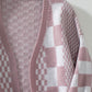 Dusty pink checkered open front cardigan with dropped shoulders, featuring a stylish and playful pattern, hanging on a hanger.