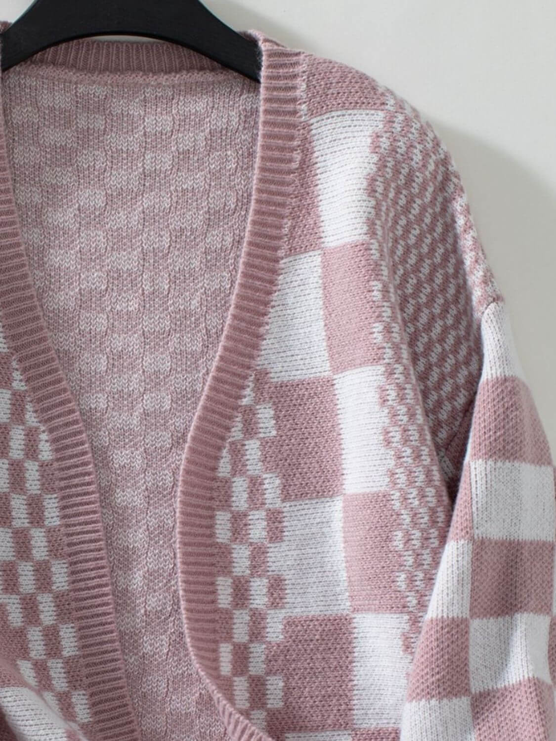 Dusty pink checkered open front cardigan with dropped shoulders, featuring a stylish and playful pattern, hanging on a hanger.