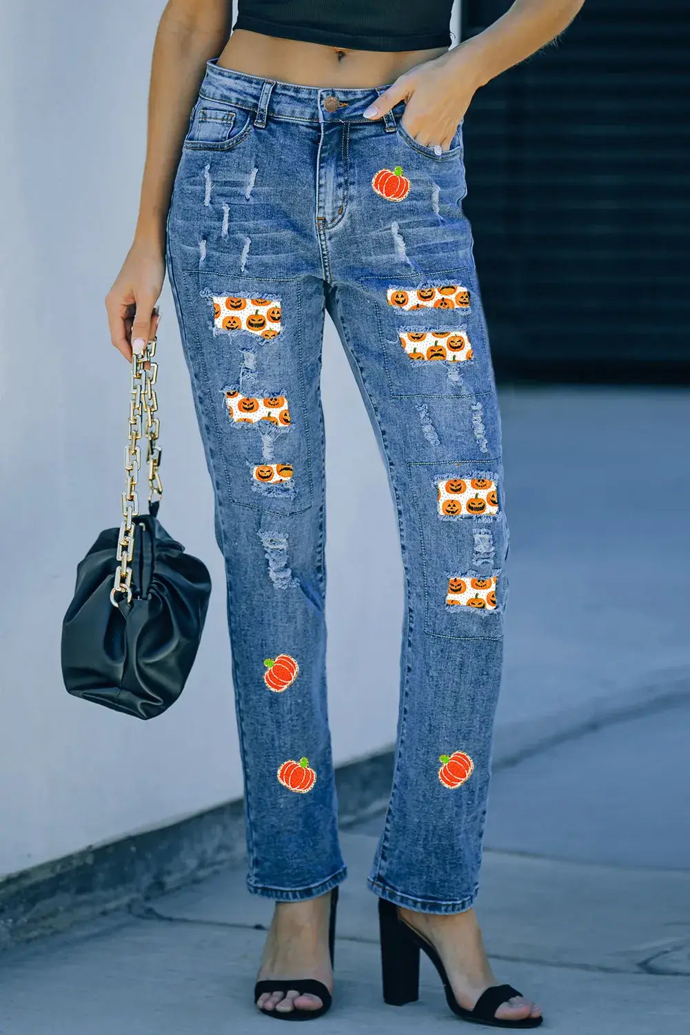 Woman wearing distressed pumpkin jeans with pockets, slightly stretchy denim with pumpkin patches and rips, styled with black top and heels.