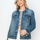 Stylish woman in a distressed button-up denim jacket over a striped top, showcasing a trendy and edgy look.