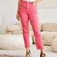 Woman wearing Crop Dylan Full Size Tummy Control High Waist Raw Hem RFM Jeans in vibrant pink, paired with a white top and black heels.