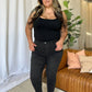 Woman wearing RFM Full Size High Rise Tummy Control Skinny Jeans standing confidently in a stylish interior.