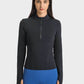 Model wearing a Millennia Half Zip Thumbhole Sleeve Sports Top in black with blue workout leggings, showcasing style and comfort.