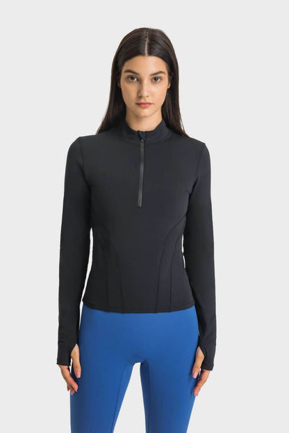 Model wearing a Millennia Half Zip Thumbhole Sleeve Sports Top in black with blue workout leggings, showcasing style and comfort.