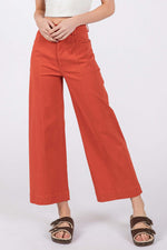 Woman wearing wide leg cropped pants in rust-orange with front pockets and adjustable button closure for a stylish and comfortable fit.