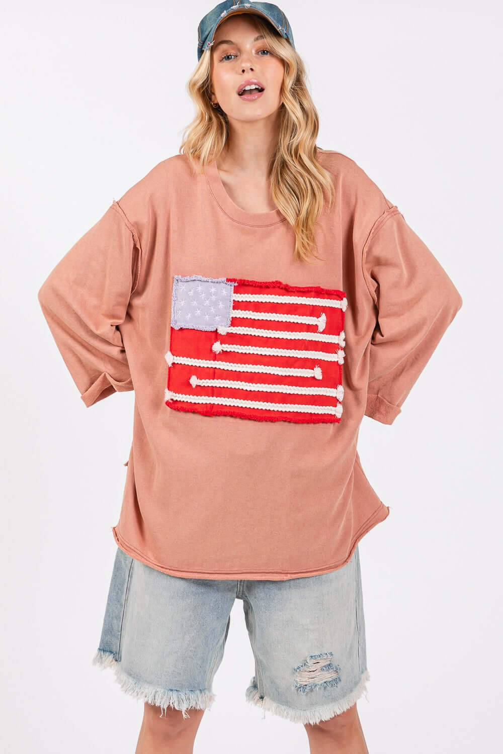 Woman wearing full size American Flag patch drop shoulder T-shirt with raw edge details, paired with distressed denim shorts.