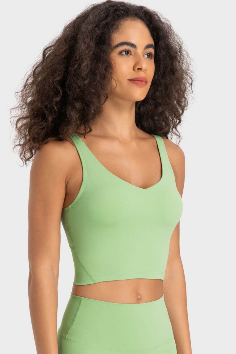 Model showcasing the Millennia Deep V-Neck Crop Sports Bra in vibrant green, perfect for stylish workouts and comfort.