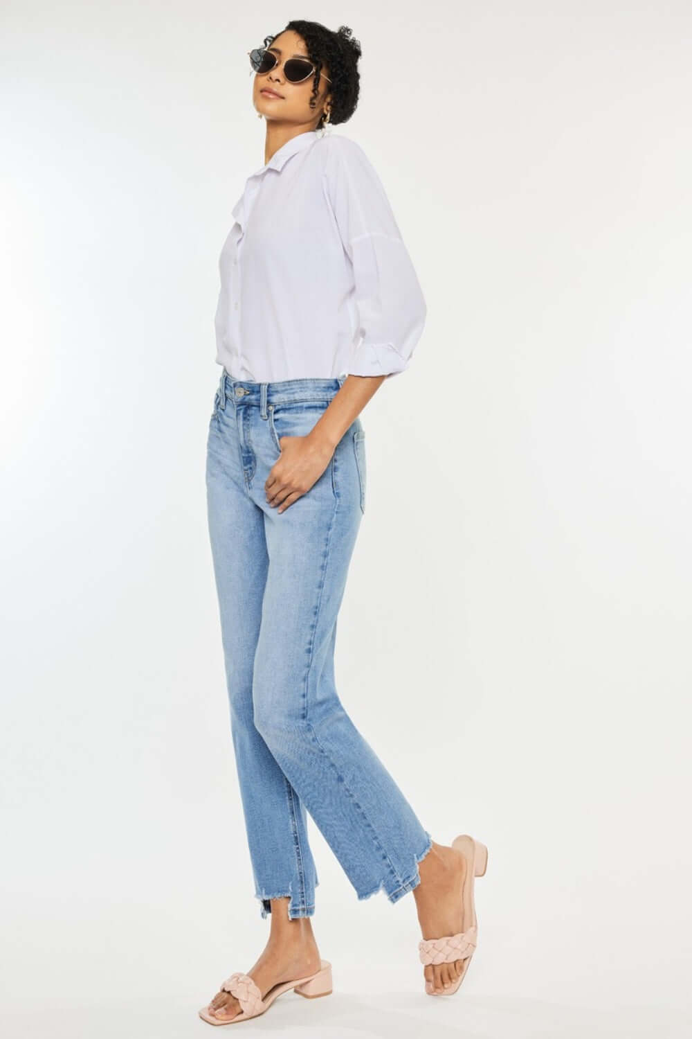 Woman wearing high waist raw hem straight jeans with a white blouse and sandals, showcasing a chic casual look.