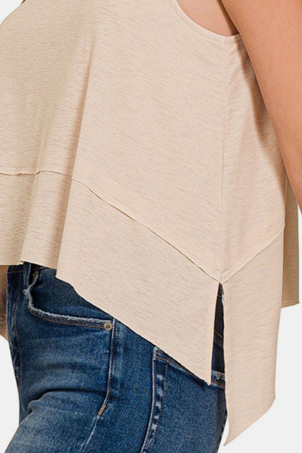 Side view of a beige exposed seam slit round neck tank paired with blue jeans.