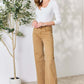 Woman wearing Fringe Hem Wide Leg Risen Jeans stands by plant, showcasing high-waisted flattering fit and trendy wide-leg design.