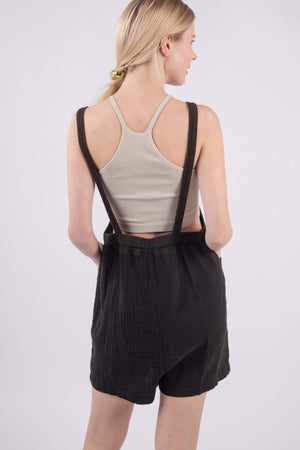 Woman wearing sleeveless double gauze overalls with pockets, showing open back and wide shoulder straps for a comfortable summer fit.