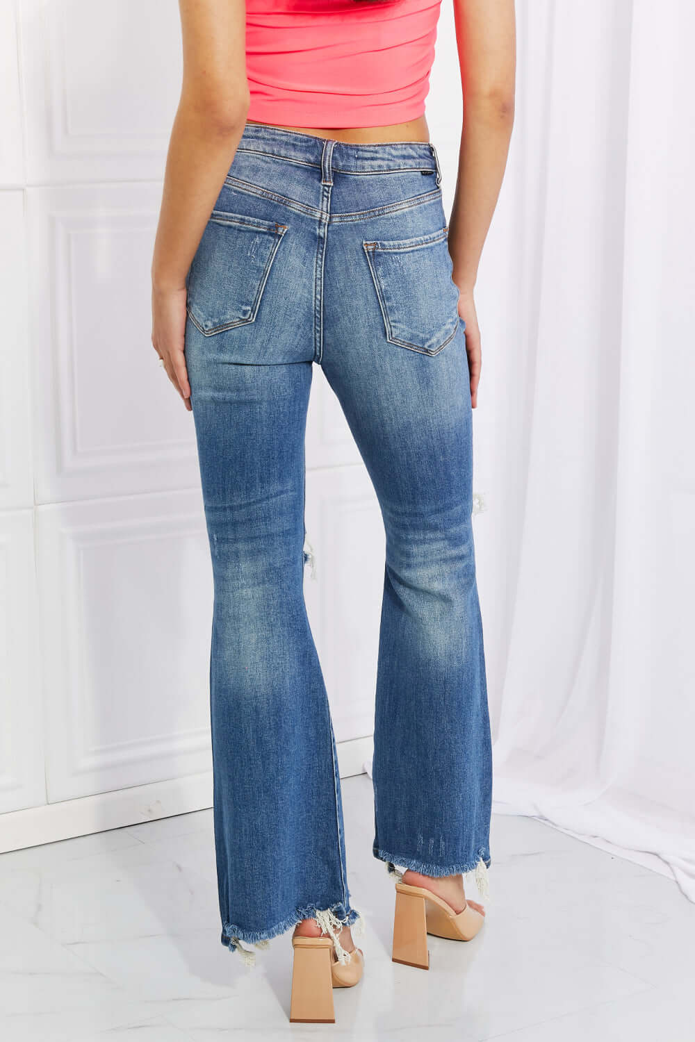 Woman wearing Risen Hazel High Rise Distressed Flare Jeans with frayed hems, showing back pocket details.