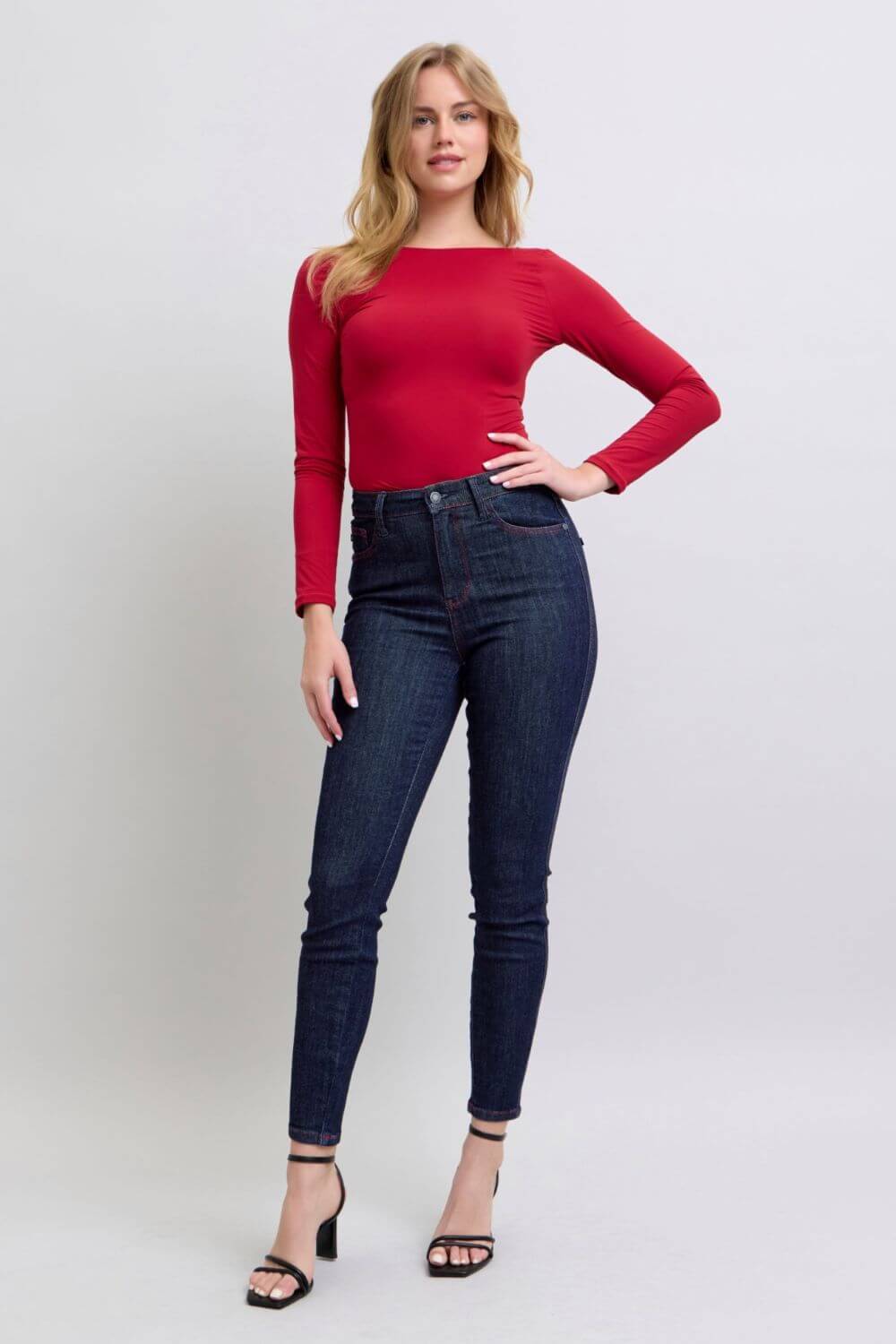 Woman wearing Judy Blue skinny jeans with heart-shaped back pockets, styled with a red top and black heels.