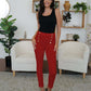 Woman wearing FAM-FAM High Waist Skinny Pants in red with decorative buttons, styled in a chic living room.