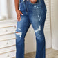 Woman wearing Judy Blue Jeans mid-rise hand sand and destroy bootcut jeans with a distressed look in front of a dresser.