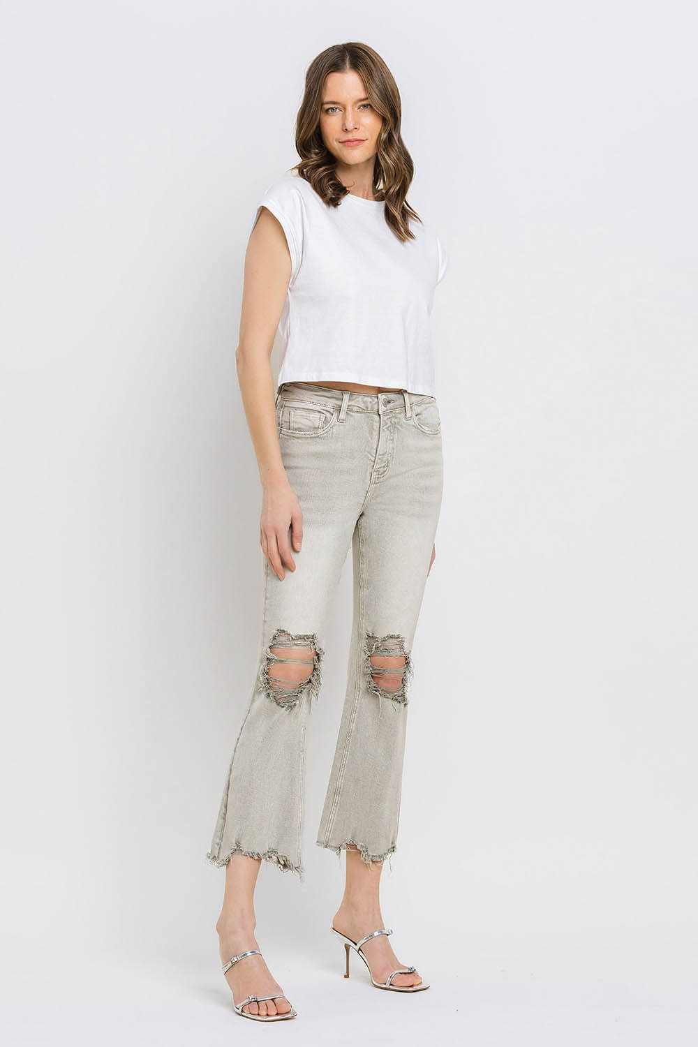 Woman wearing Lovervet Distressed Raw Hem Cropped Flare Jeans with ripped knees and a white crop top, styled with strappy sandals.