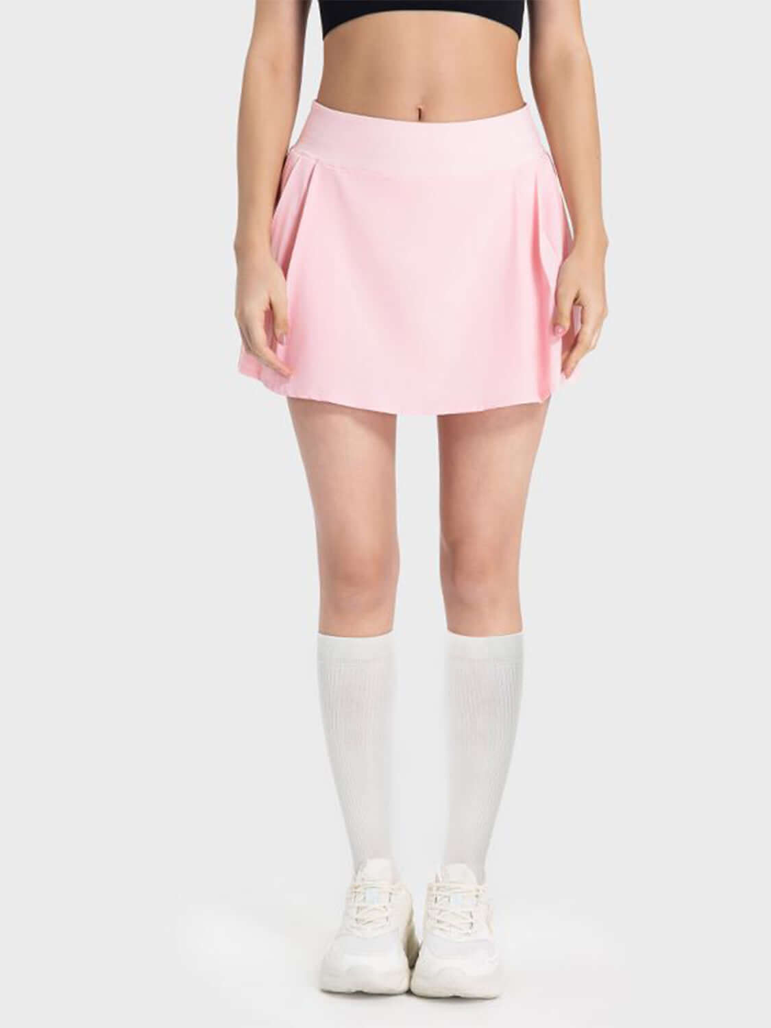 Stylish woman wearing a pink pleated active skirt with a mid-rise waist and knee-high socks. Perfect for sporty and chic looks!