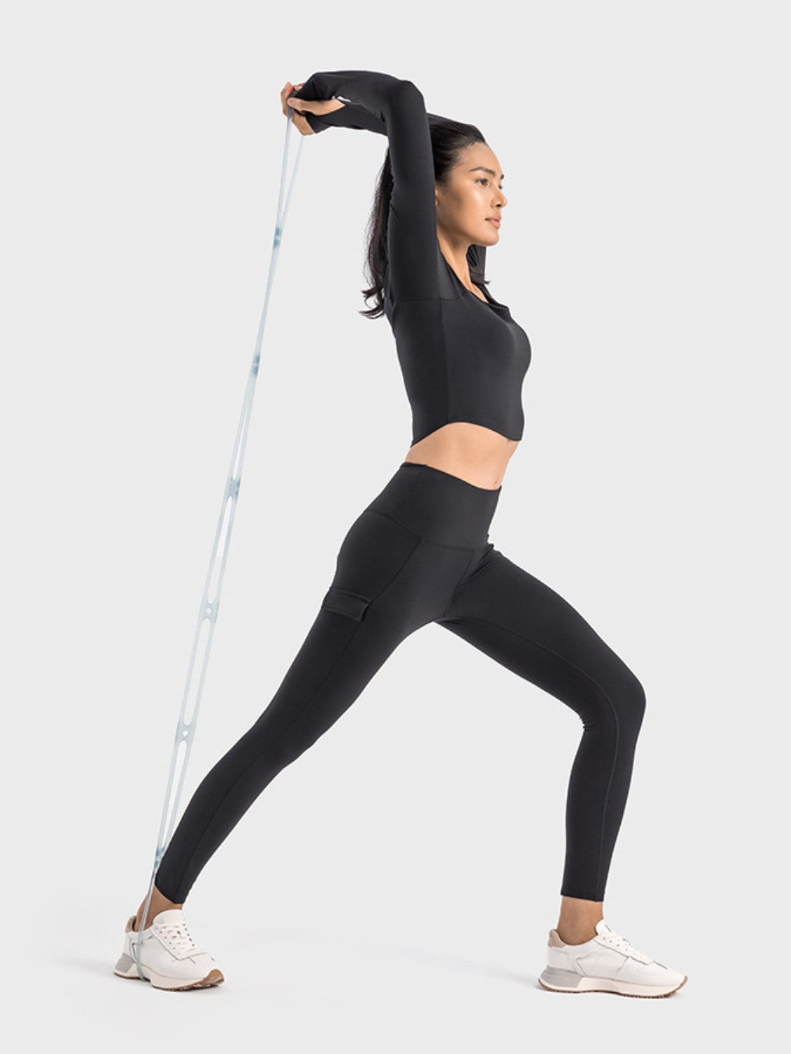 Woman in black Millennia sports leggings stretching with resistance band, showcasing activewear versatility and style.