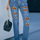 Woman wearing distressed pumpkin pattern jeans with pockets and holding black handbag. Slightly stretchy material with ripped details.