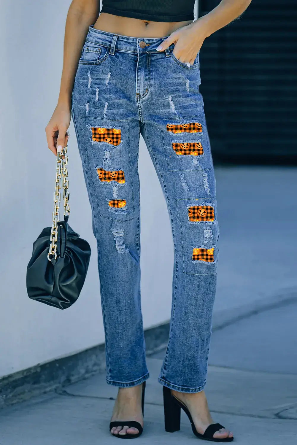 Woman wearing distressed pumpkin pattern jeans with pockets and holding black handbag. Slightly stretchy material with ripped details.