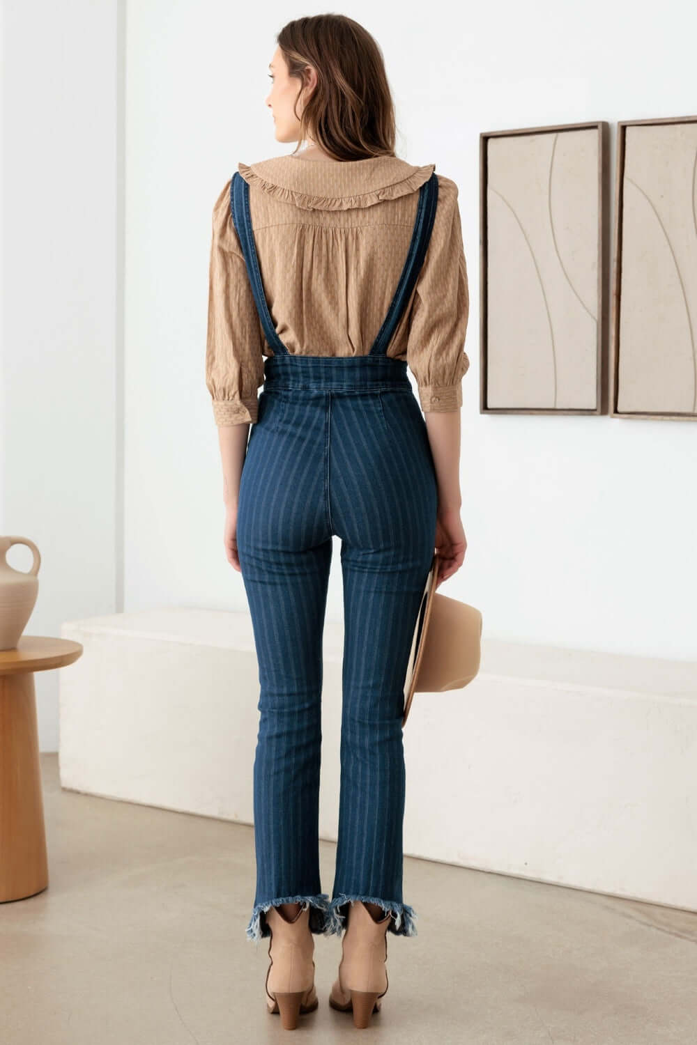 Woman wearing striped stretched suspender denim overalls with high waist design, front pockets, and destroyed hem for a retro-inspired style