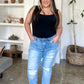 Woman wearing Judy Blue distressed straight jeans with patch pockets, black tank top, standing in minimalist living room.