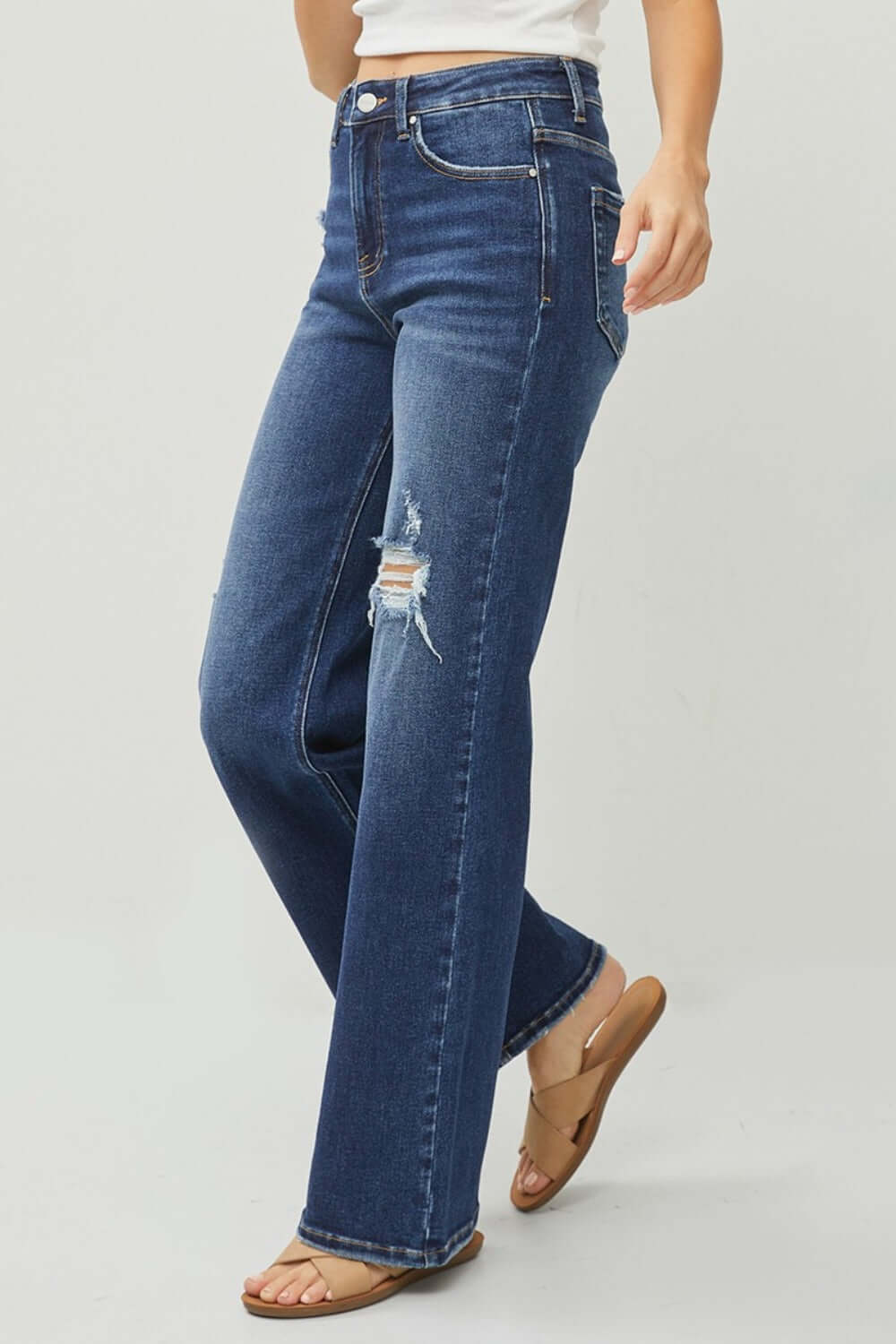 Woman wearing RISEN Full Size High Rise Distressed Wide Leg Jeans with slight stretch and pocketed design in dark wash.