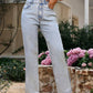 Model wearing Bella Road Side Slit Straight Leg Jeans in light wash, showcasing pockets and stylish side slits amidst blooming flowers.