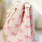 Pink ribbon bowknot pattern crossbody bucket bag with drawstring closure and white strap on a light background.