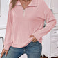 Woman wearing pink striped half zip long sleeve t-shirt with slightly stretchy fabric, styled with blue jeans in a casual indoor setting.