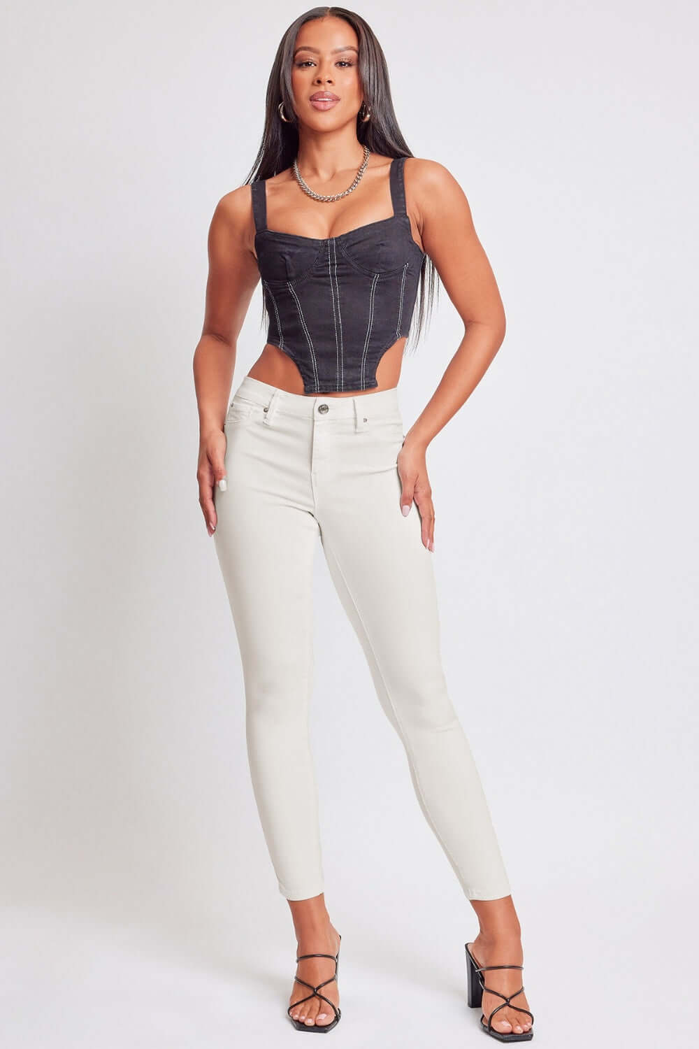 Woman wearing YMI Hyperstretch Mid-Rise Skinny Jeans in white, paired with a black corset top, styled for a trendy and modern look.