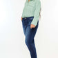 Woman wearing high rise frayed ankle skinny jeans and a light green top, showcasing trendy and stylish wardrobe choice.