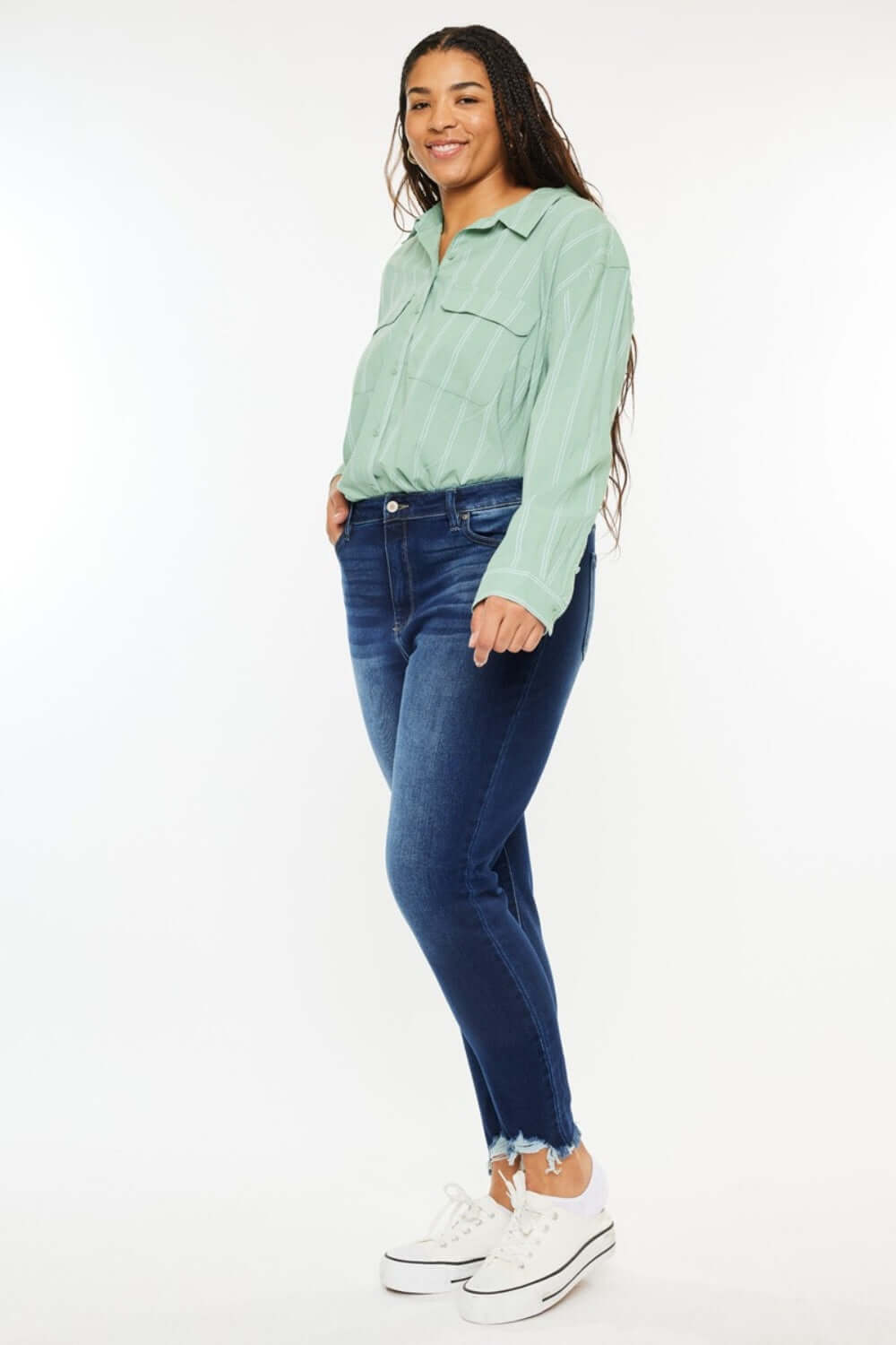 Woman wearing high rise frayed ankle skinny jeans and a light green top, showcasing trendy and stylish wardrobe choice.