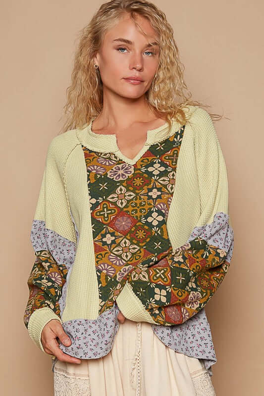 Trendy woman in a notched raglan sleeve knit top featuring exposed seams and vibrant prints, perfect for a stylish look.