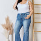 Woman wearing Risen Jeans High Rise Ankle Flare Jeans with white top, posing confidently indoors by decorative vases and a wooden ladder