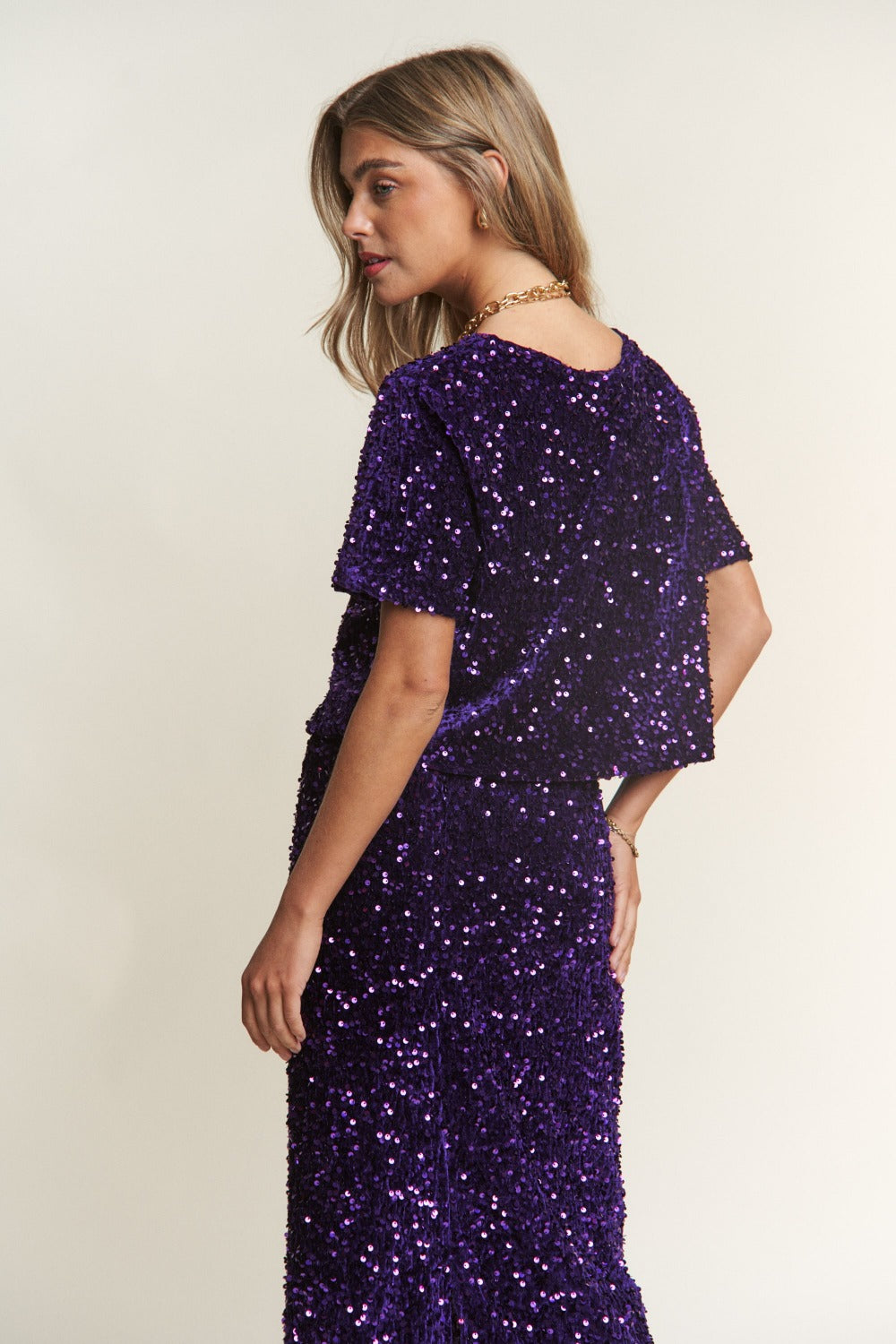 Woman wearing a purple sequin short sleeve crop T-shirt, sparkling under the light, showcasing a trendy and festive style.