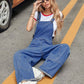 Woman in Bella Road Wide Strap Denim Overalls sitting on the street next to a car, showcasing wide-leg design and casual style.