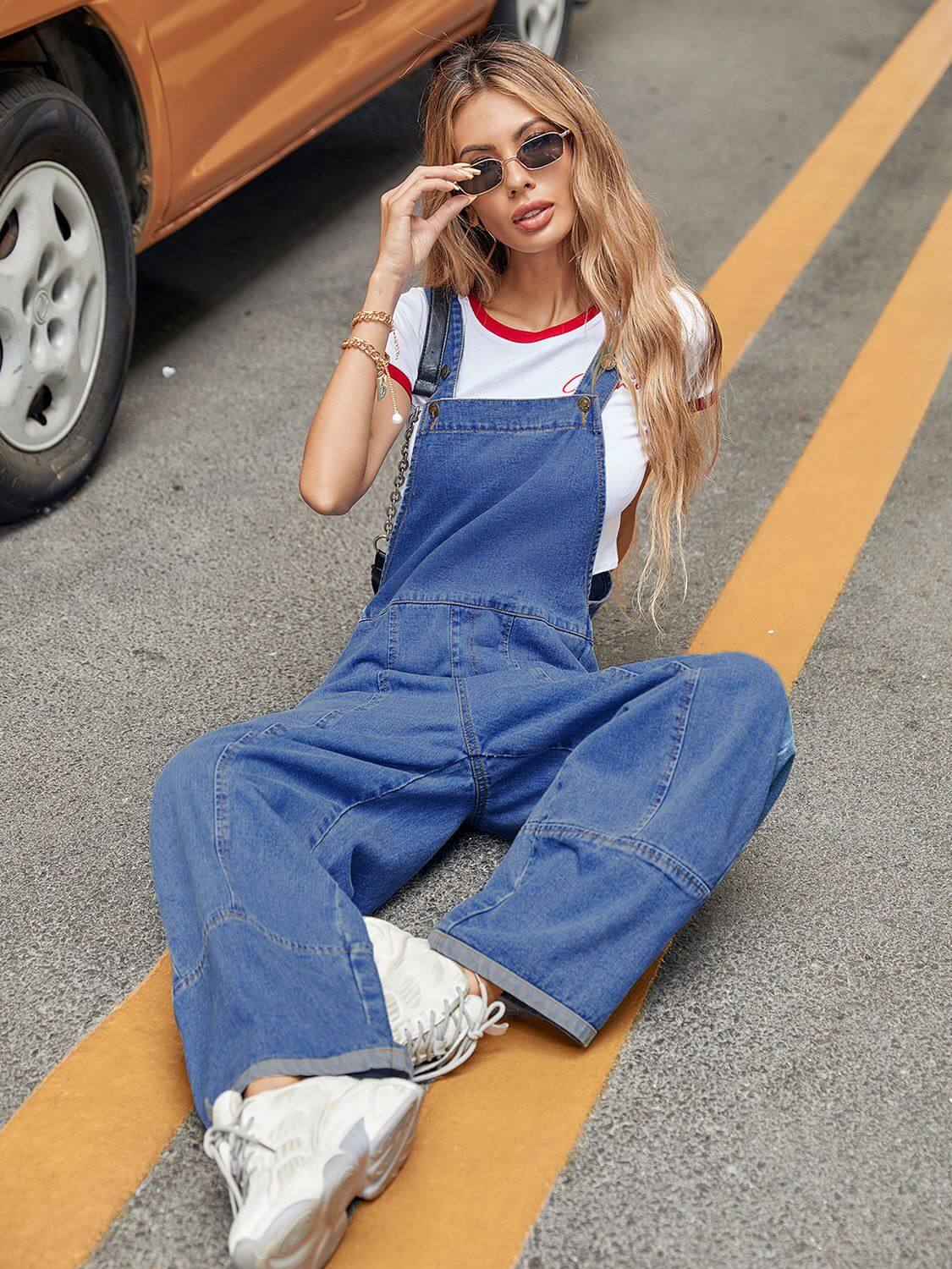 Woman in Bella Road Wide Strap Denim Overalls sitting on the street next to a car, showcasing wide-leg design and casual style.