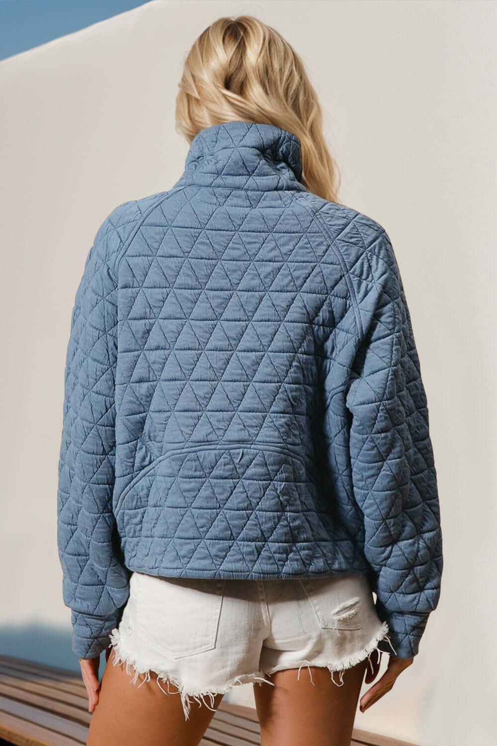 Woman wearing blue quilted half zip long sleeve sweatshirt with a pocket and white shorts, showcasing cozy chic style.