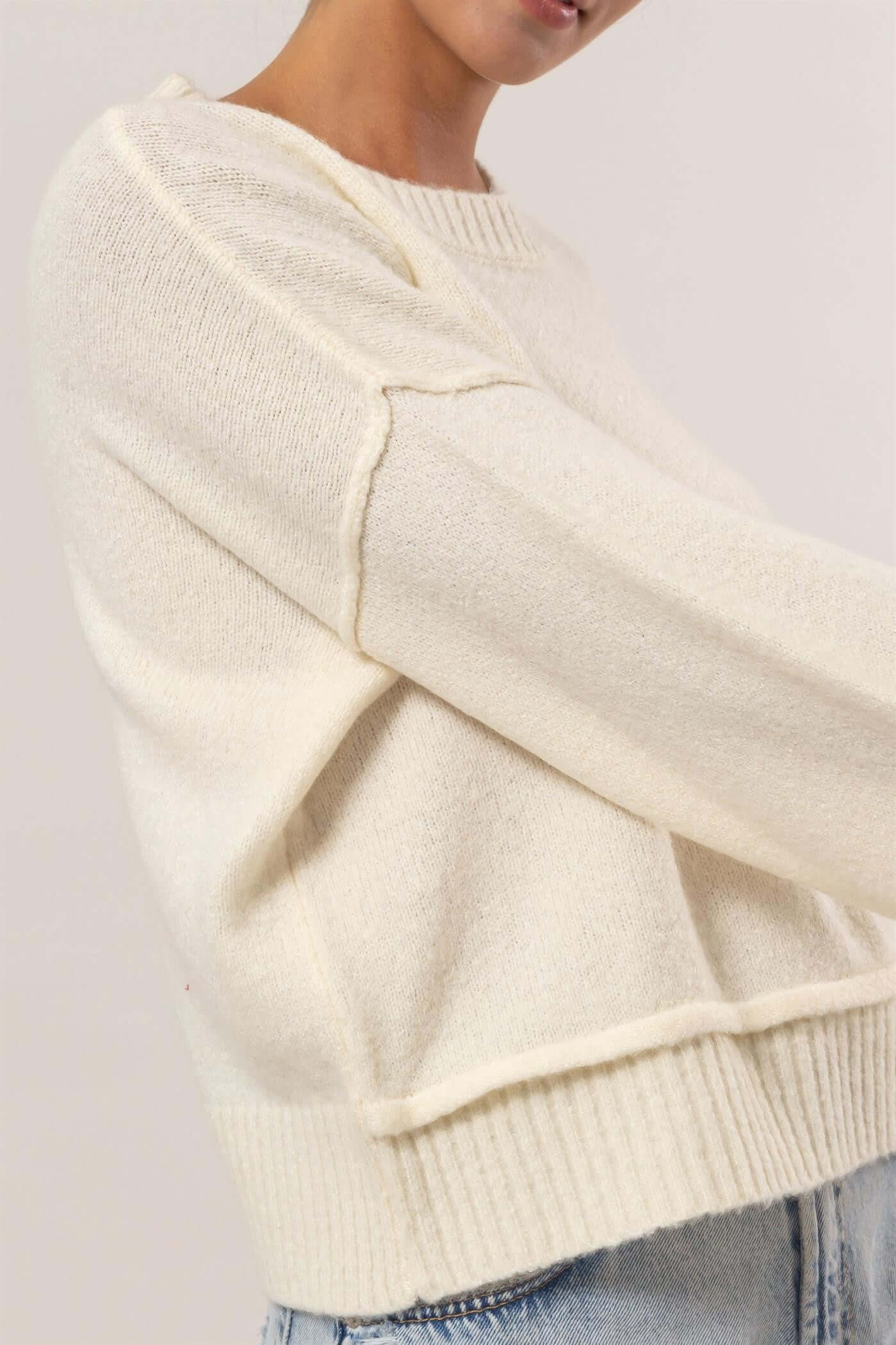 Model showcasing a cream-colored ribbed sweater with dropped shoulders, perfect for a stylish and relaxed look.