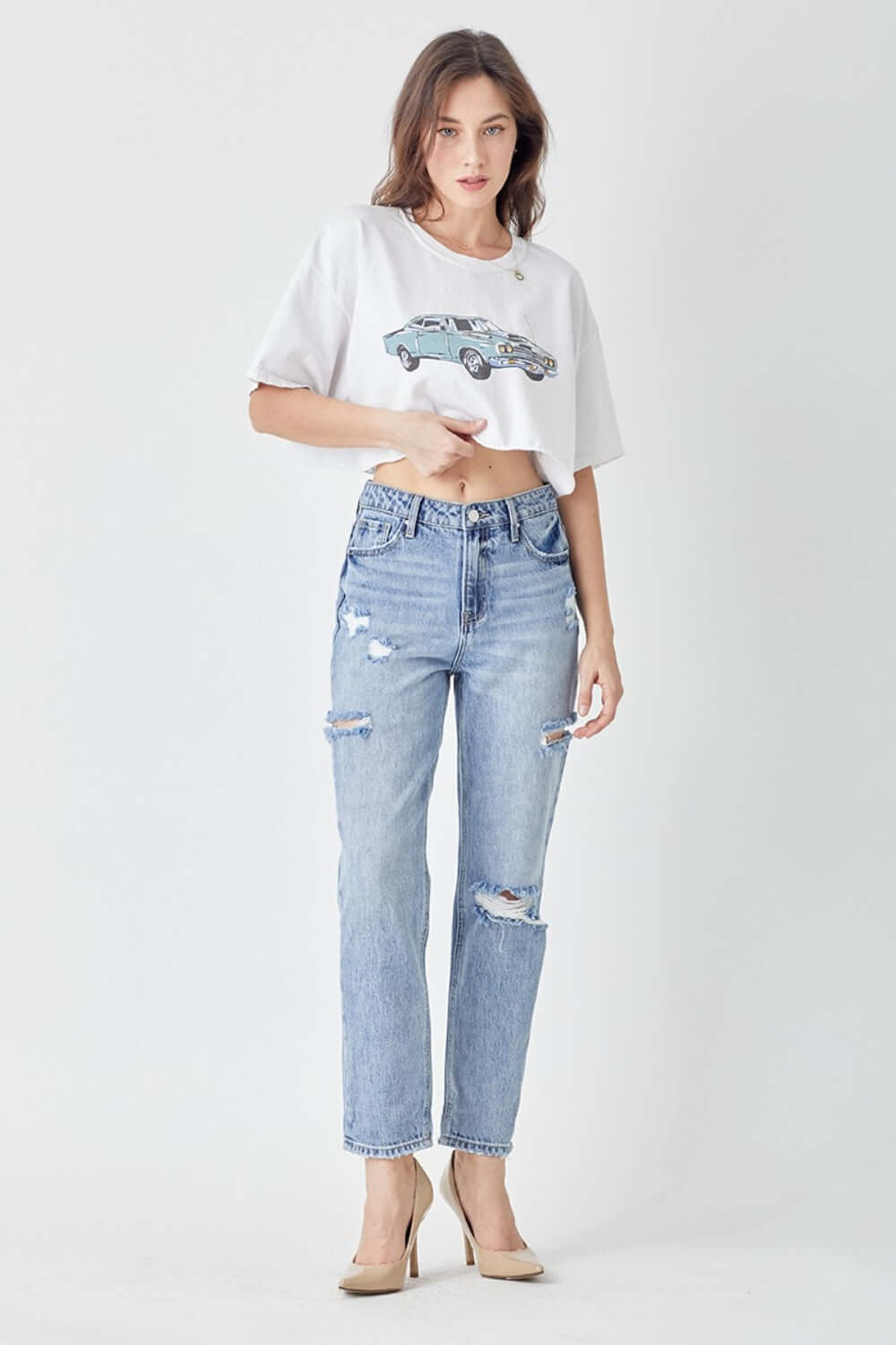 Woman wearing Risen Distressed Slim Cropped Jeans paired with a graphic tee and heels, showcasing the edgy distressed detailing and flattering fit.