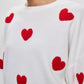 Cozy white sweater with red heart details and round neck, featuring dropped shoulders. Perfect for a sweet and stylish look.