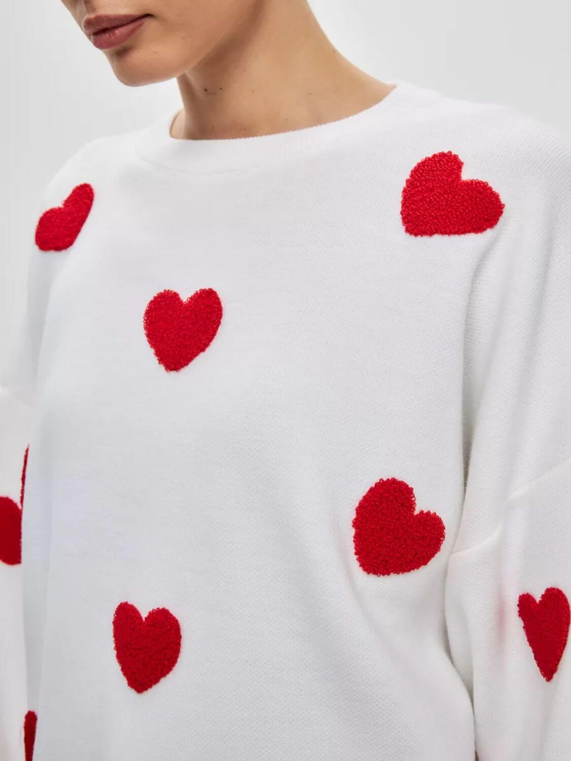 Cozy white sweater with red heart details and round neck, featuring dropped shoulders. Perfect for a sweet and stylish look.