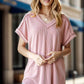 Woman wearing Exposed Seam Short Sleeve Ribbed Top in light pink, stylish and modern design, paired with jeans, in an urban setting.