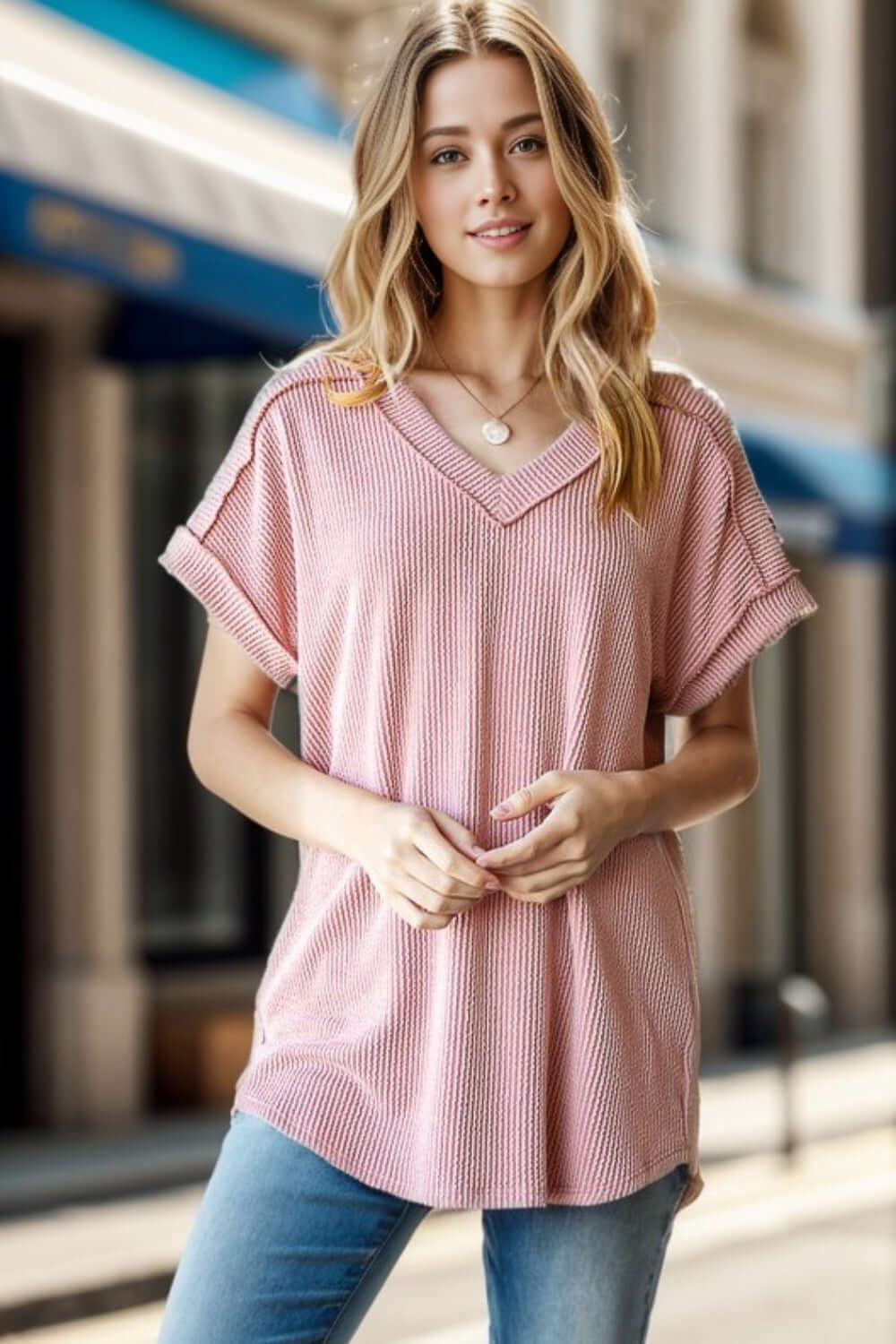 Woman wearing Exposed Seam Short Sleeve Ribbed Top in light pink, stylish and modern design, paired with jeans, in an urban setting.